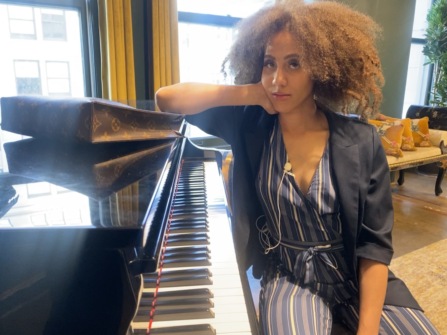 IREIGN leaning on a grand piano in a sunlit room, mid creative process