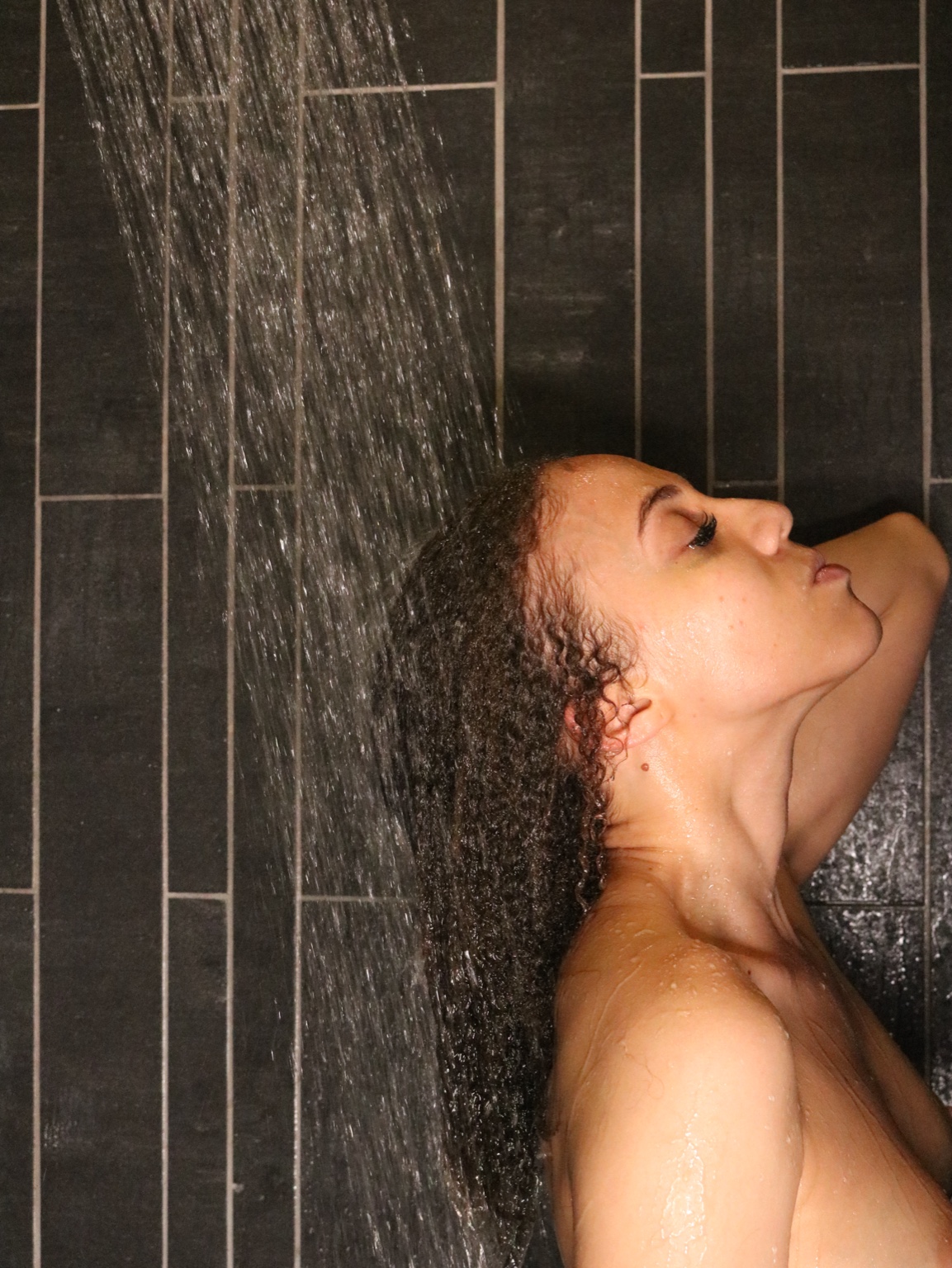 Moody black-tiled portrait of IREIGN beneath falling water