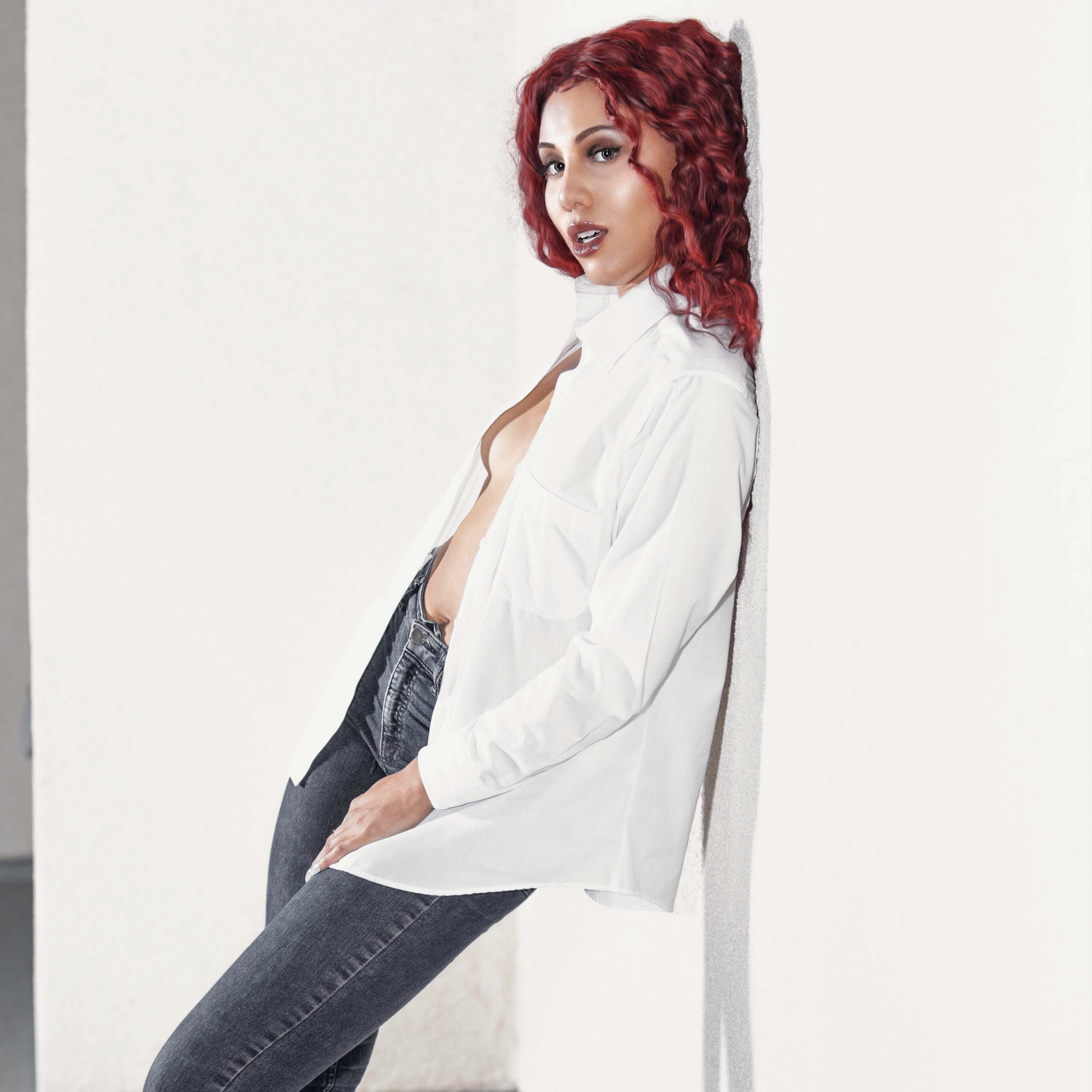 IREIGN with red hair leaning against a white wall in an open white shirt