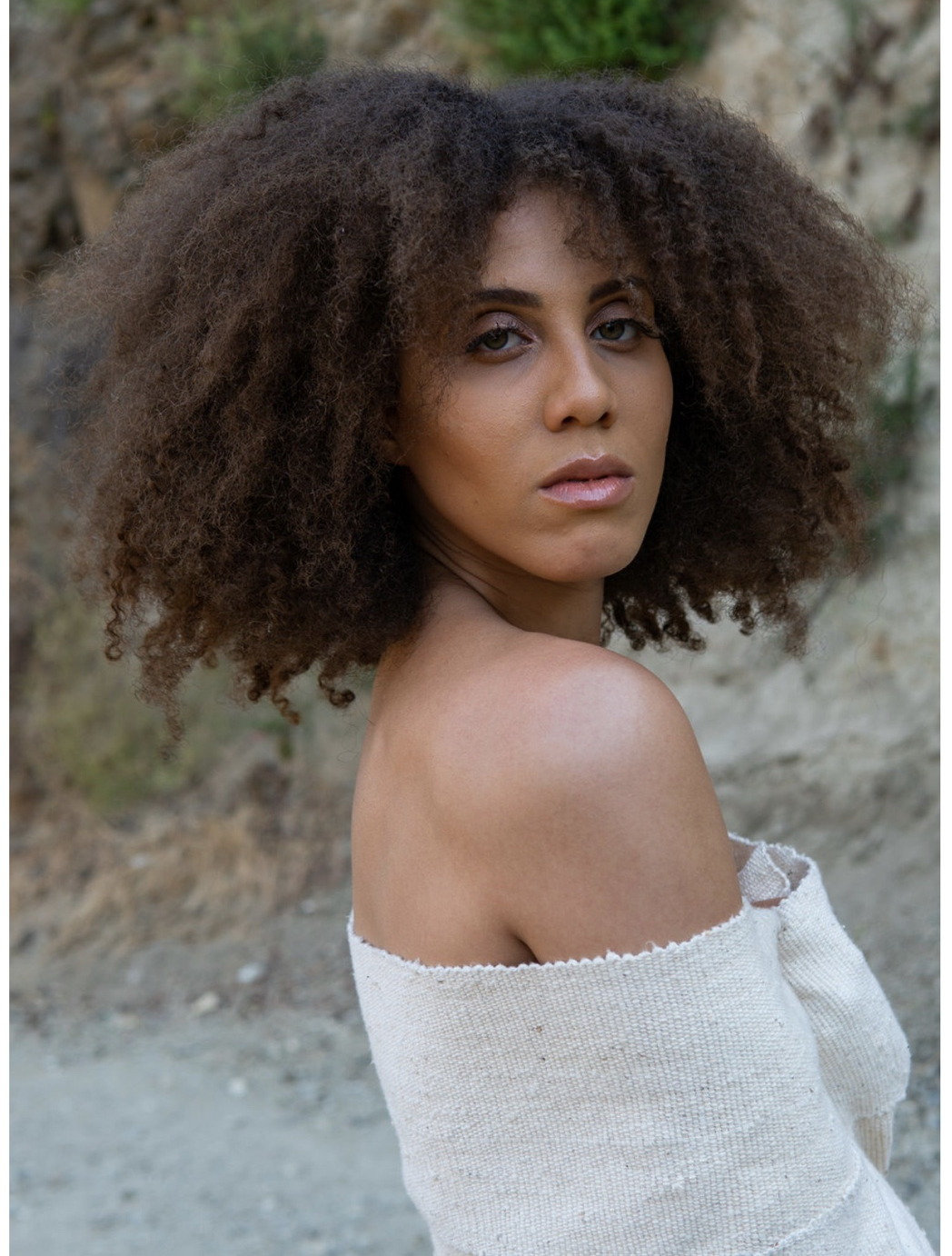 IREIGN with natural curls looking over her shoulder outdoors